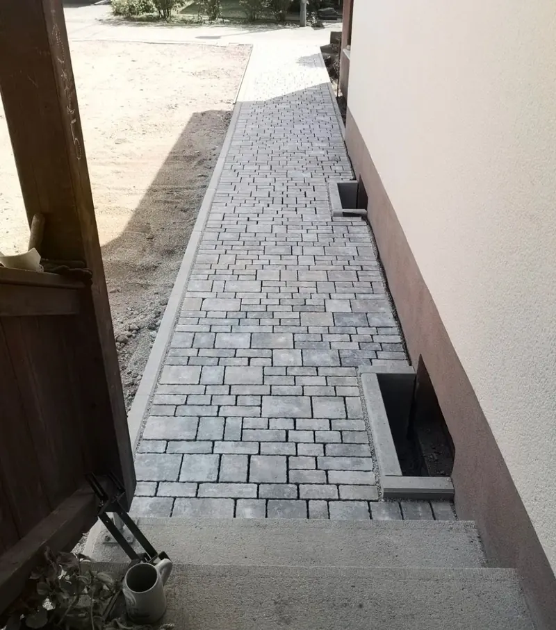 Seitenweg am Haus aus grauem Pflaster mit eingefasstem Lichtschacht