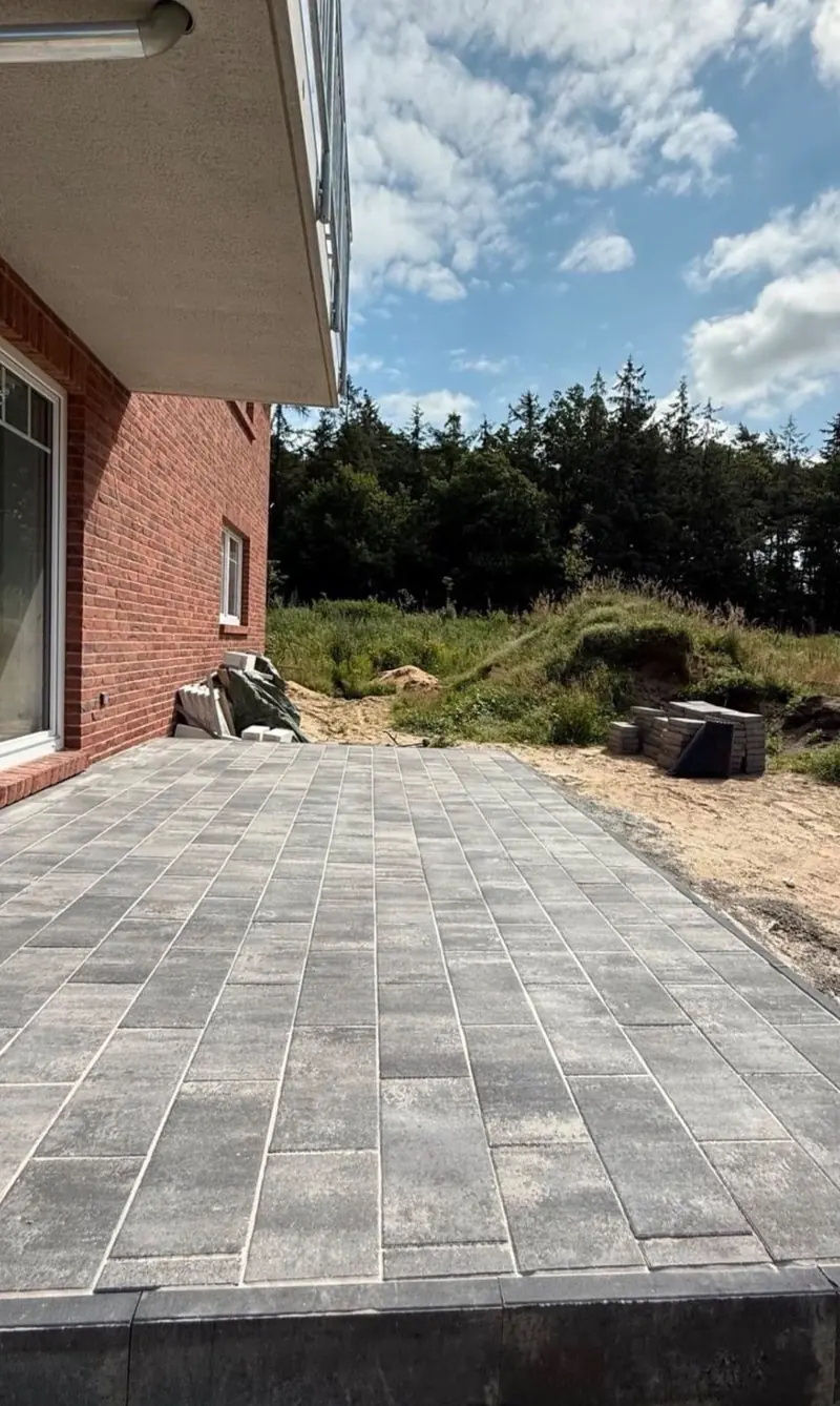 Neue Terrasse aus grauem Betonpflaster an einem Klinkerhaus