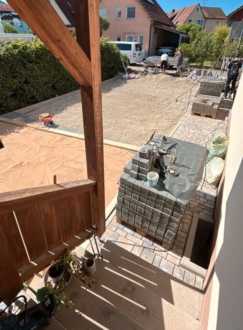Pflasterarbeiten unter einer Holzpergola, das Pflaster liegt auf Paletten bereit